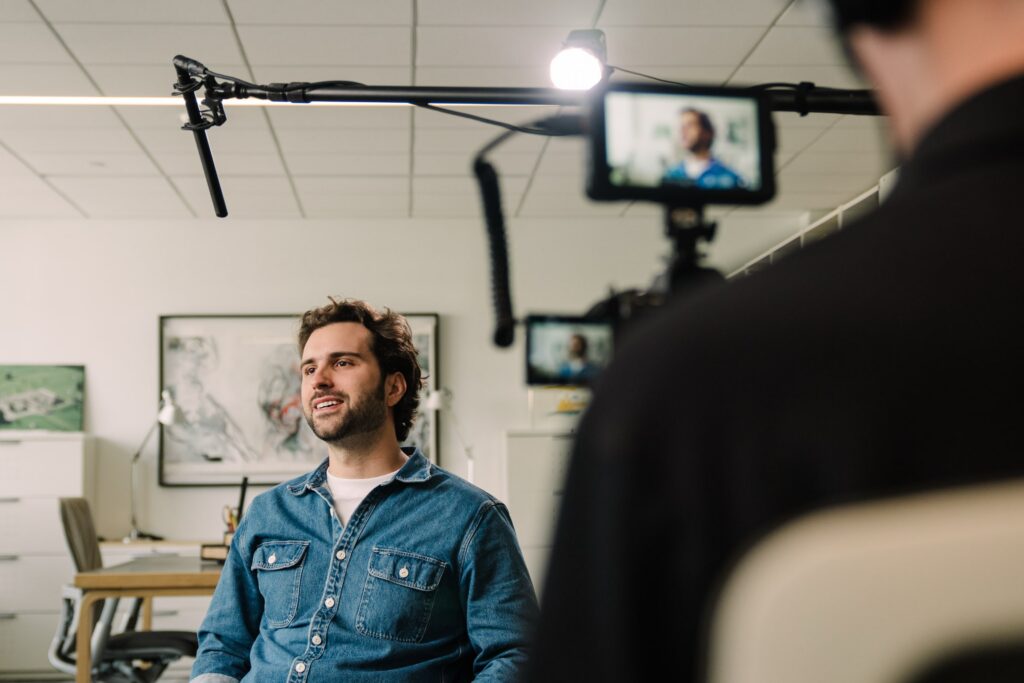 Collin Maloney, Project Manager at Blackburn Architecture, sits for a documentary-style interview at the firm's Washington, D.C. office during production of the Blackburn brand film. Storyteller Studios camera, boom microphone, and lighting visible in frame.