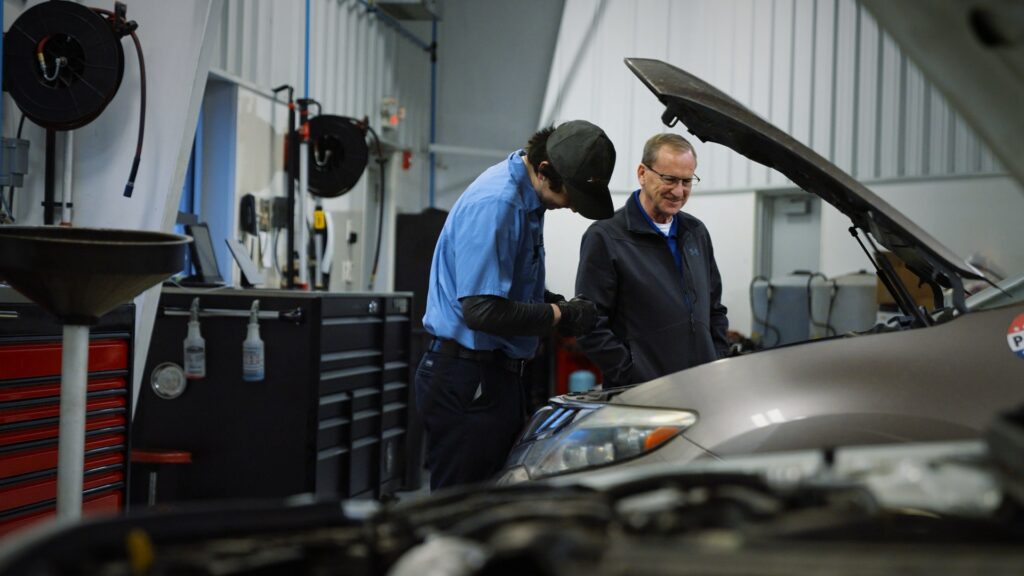 A mechanic works on a vehicle while a colleague observes at Floyd Imports, the family-owned foreign car repair shop in Springfield, Illinois, photographed during a Storyteller Studios brand film shoot.