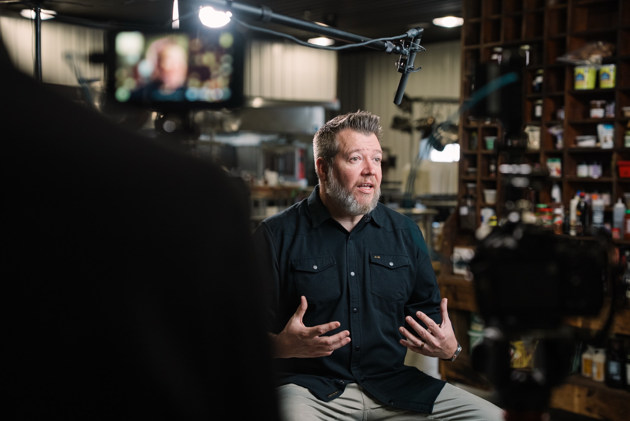 Man being interviewed during documentary-style video production, with professional lighting and boom microphone visible on set