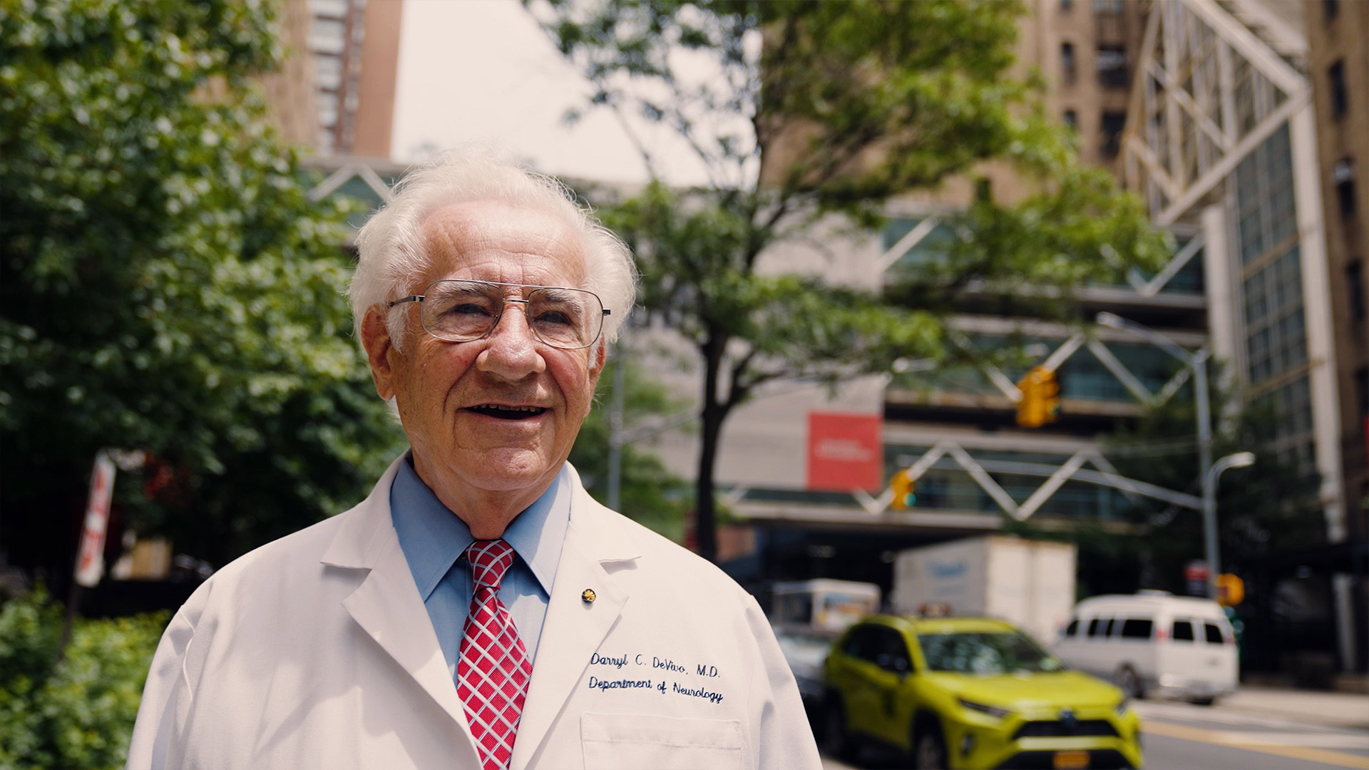 an elderly doctor walks the streets of new york in a lab coat