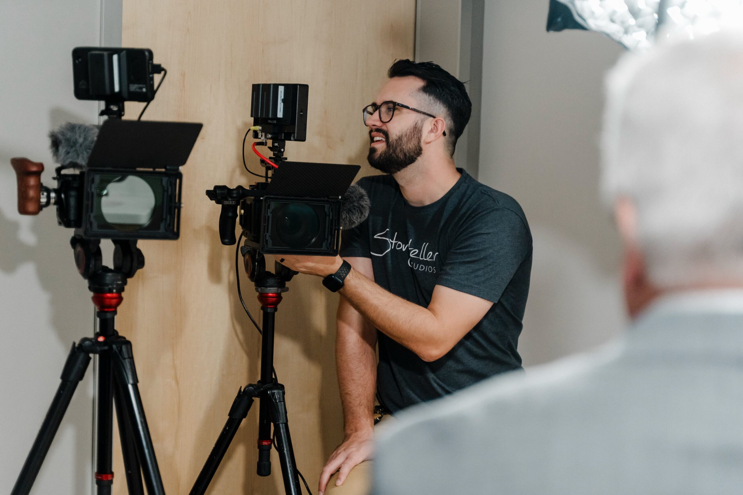 a videographer works with two cameras and lights with a corporate client in the foreground