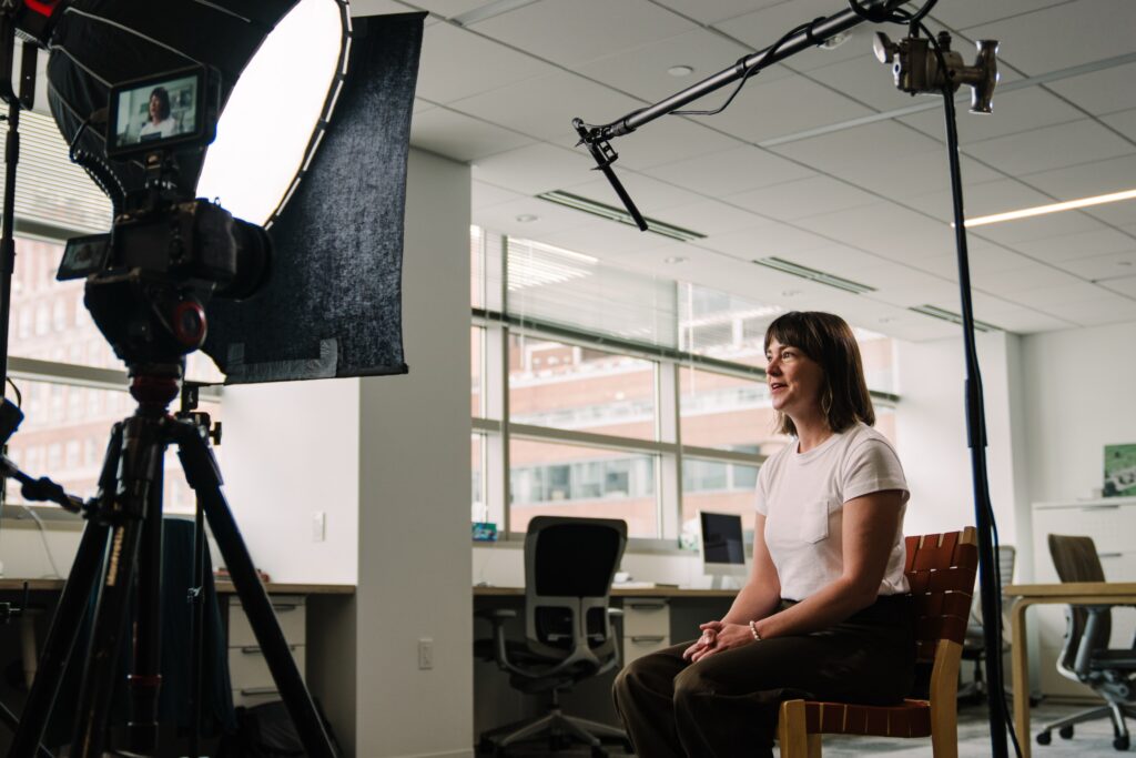 Professional video production setup showing camera, lighting equipment, and boom microphone positioned for corporate interview in modern office.