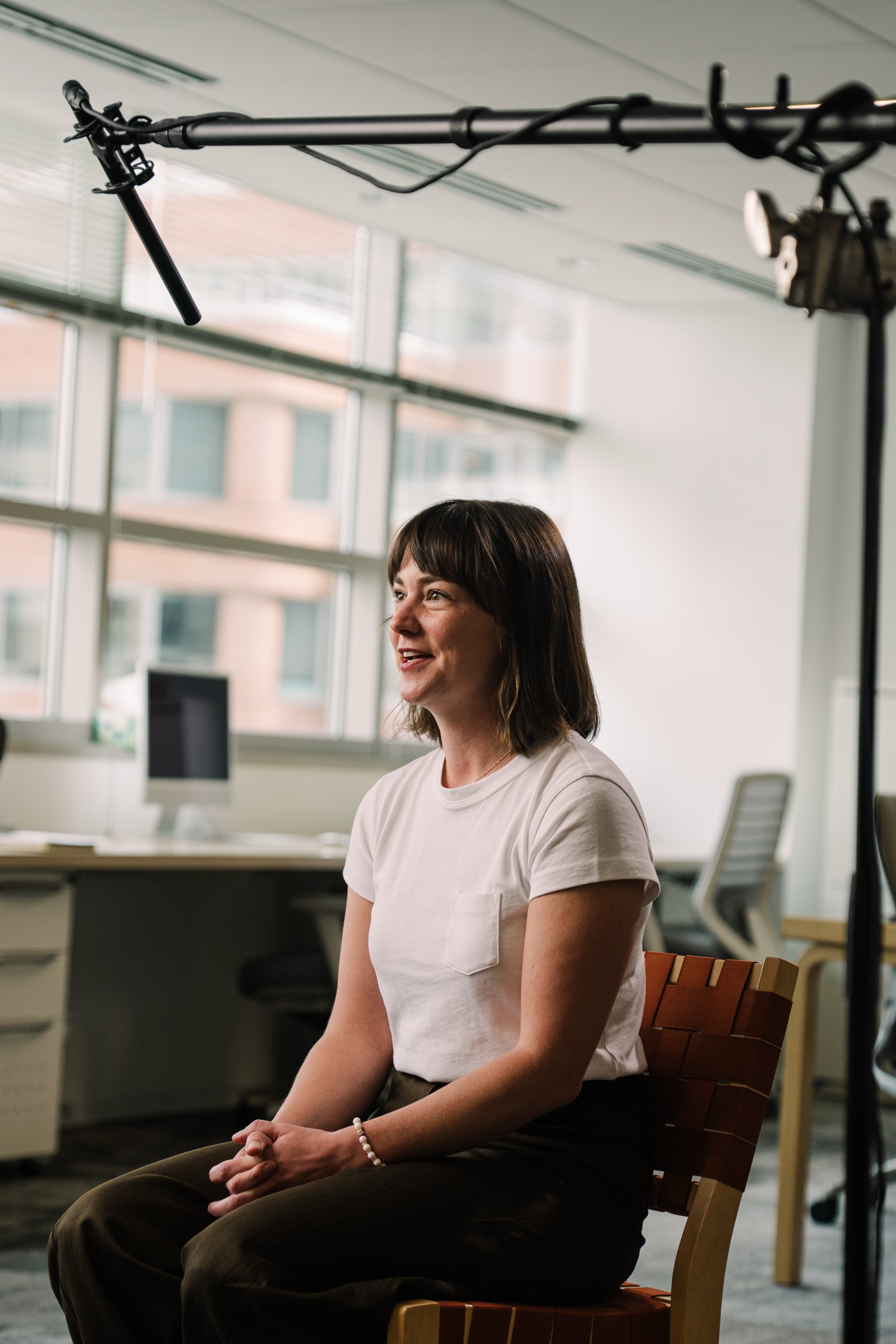 Professional woman being interviewed in modern corporate office with professional video production lighting and microphone setup visible.