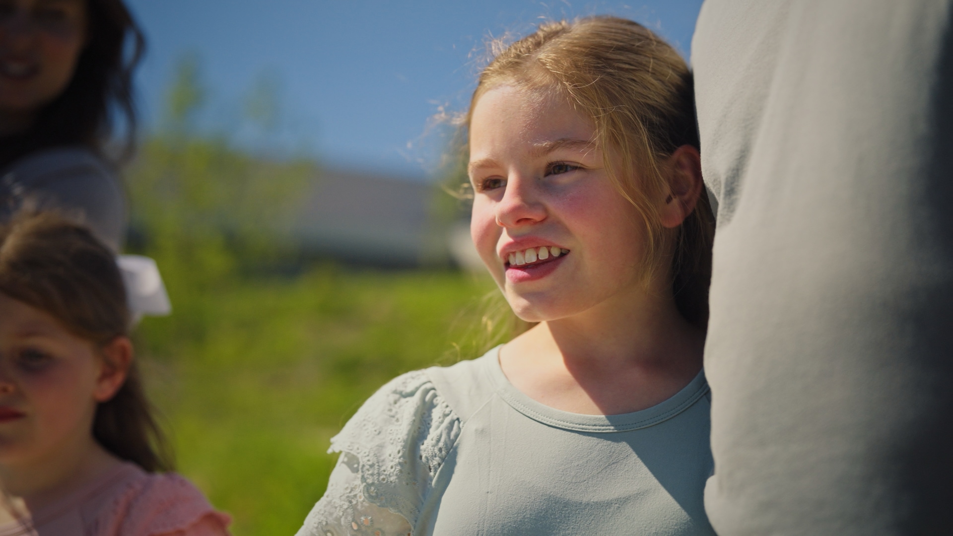 Amelia Darch smiles in the sunshine with her family behind her, a still from the National Children's Cancer Society's fundraising film.