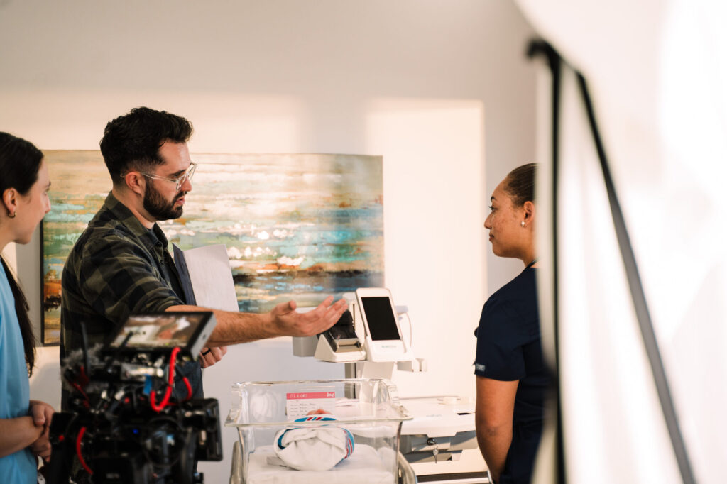 Storyteller Studios director Chris Costello blocks a scene with an actor and a prop baby on the hospital set built for the IDPH PSA, newborn hearing screening device in frame